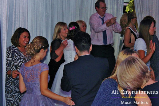 A vibrant crowd of wedding guests dancing enthusiastically at a wedding disco in Crosby, Liverpool. The scene is filled with colorful lighting and joyful expressions as people of all ages move to the music. The lively atmosphere was expertly created by Alt. Entertainments, a Wedding DJ, Mobile DJ, Disco & Events Company.
