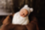 newborn baby with a white hat in a clothed basket