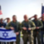 Israeli combat soldiers stand together with weapons, a small smile on their faces, behind