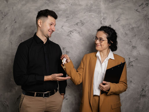 A female agent handing a house key to a male in black suit.