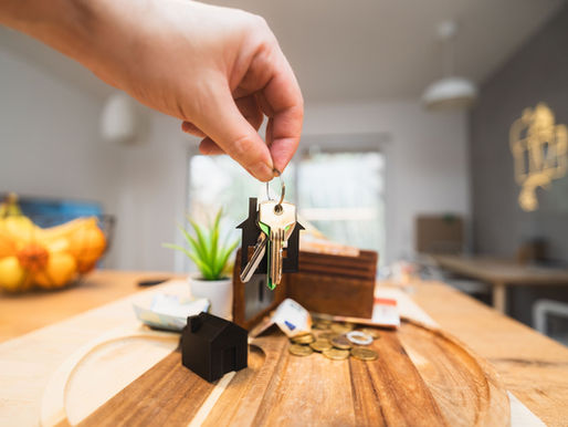 A hand holding out a house key towards scattered coins on a table.