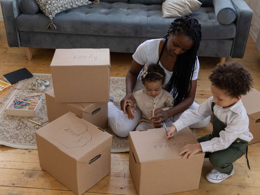 A mother sitting on the floor with her two kids, while fixing house moving boxes.