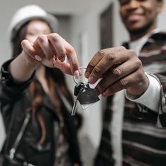 A male and female wearing hard hats holding up a house key together.