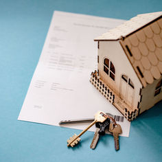 A miniature house model on top of a financial document with a house key.