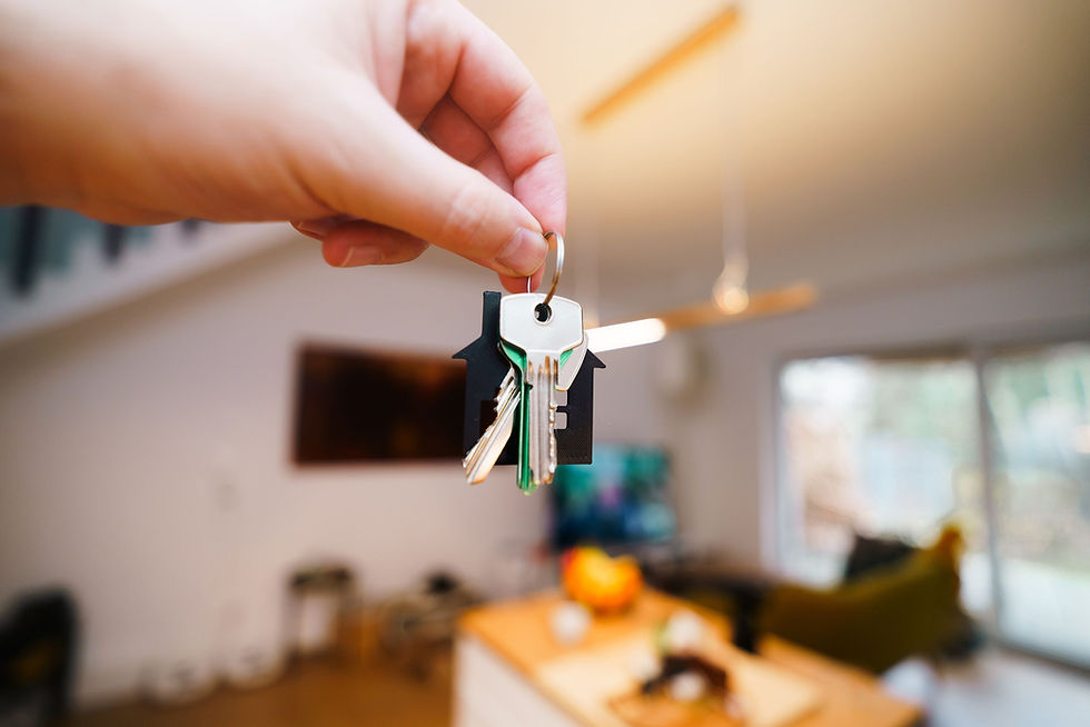 A hand holding out a house key towards a living room.