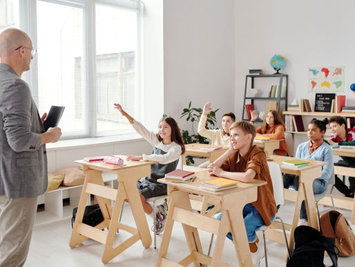 A male teacher standing in front of young students inside a classroom.