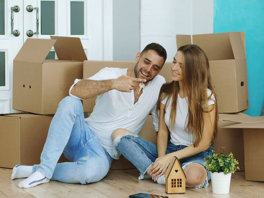 A couple sitting on the floor surrounded by house moving boxes.