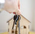 A hand holding out a house key towards a miniature house model.