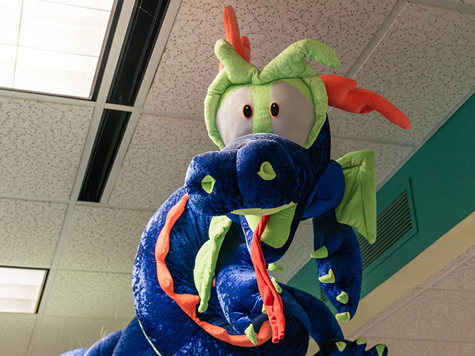 Un gran dragón de peluche azul y verde con detalles naranjas cuelga del techo.