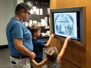 A man and two young children in the Rolland Center looking at an image related to President Lincoln.