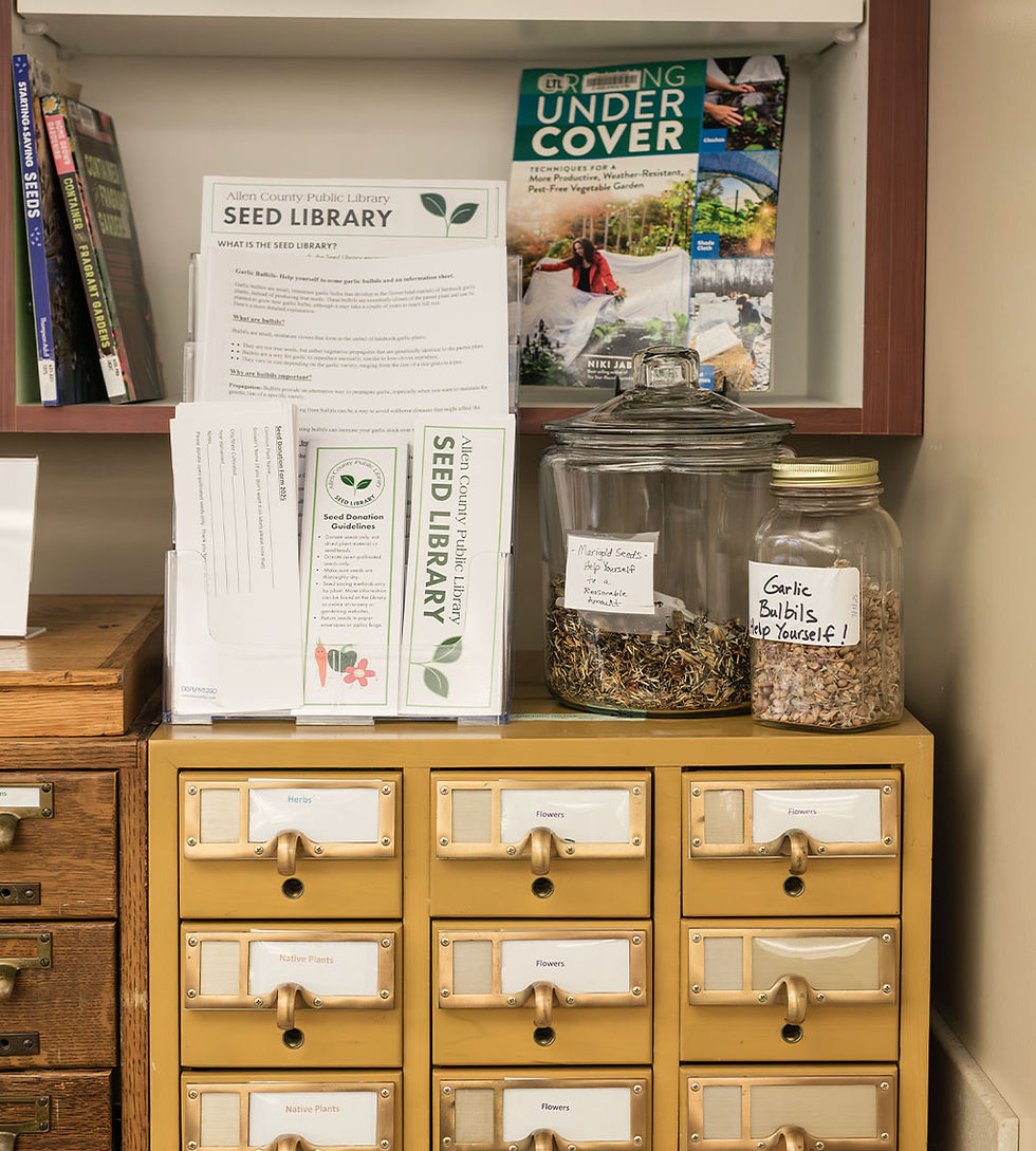 Seed library display on a vintage card catalog with brochures and two jars labeled ‘Marigold Seeds’ and ‘Garlic Bulbils.’