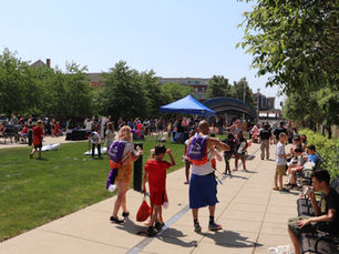 Summer Meals Kick-Off participants walking around on the Main Library Plaza. Some are playing cornhole, some are eating.