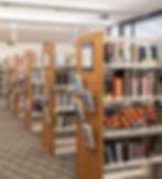 Library interior with aisles of bookshelves filled with colorful books, and wooden dividers displaying featured books.