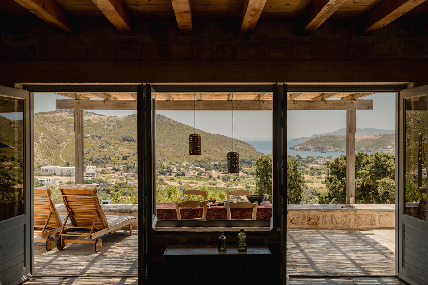 Traditional stone house interior with large glass doors opening to a terrace and panoramic mountain views.