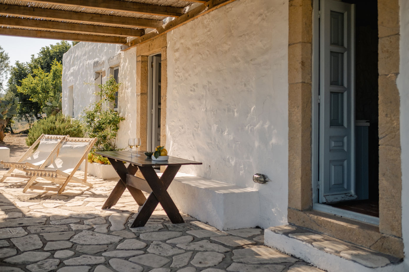 Traditional whitewashed house with shaded terrace, sun loungers, and outdoor dining table.