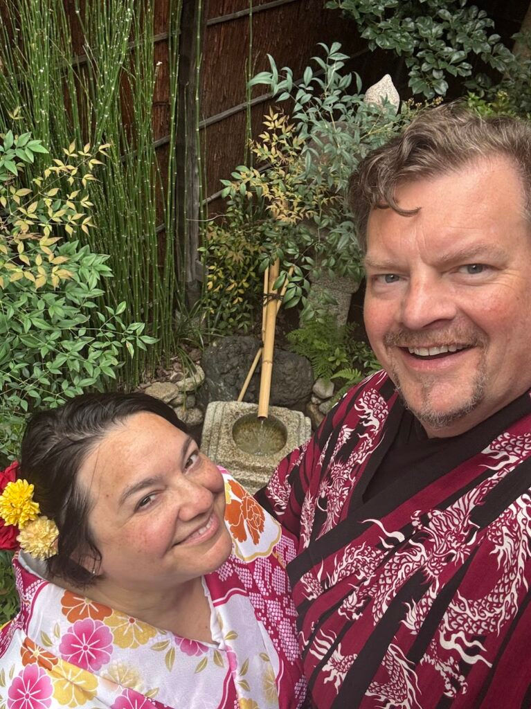 Sharon and Robert wearing colorful kimono in a lush Japanese garden. 