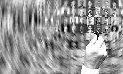 A man holds a magnifying glass over the photos of job candidates