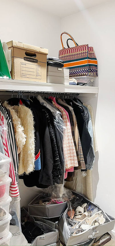 Small, disorganized closet filled with clothes, bags, and storage boxes.