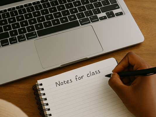 Writing in notebook next to laptop