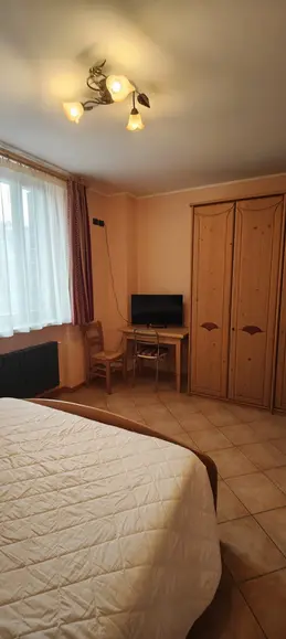 Interno di una camera con letto, armadio in legno e TV.