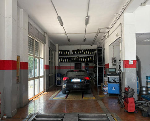 Interno dell'officina meccanica con auto nera su ponte sollevatore.