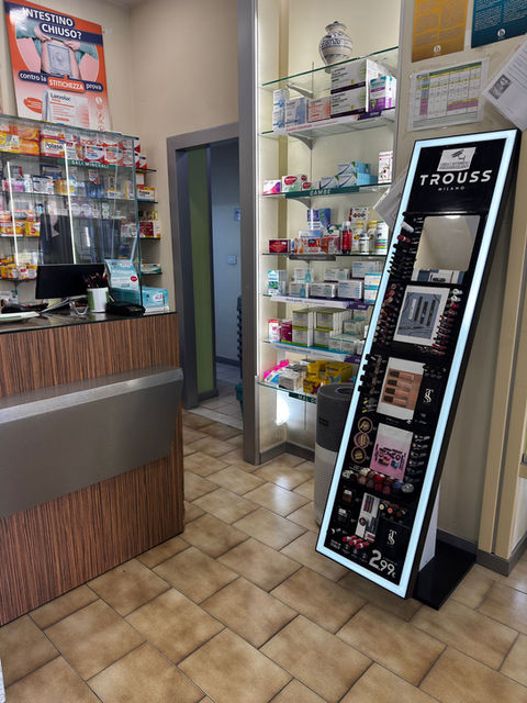 Interno farmacia con bancone e scaffali di prodotti esposti.