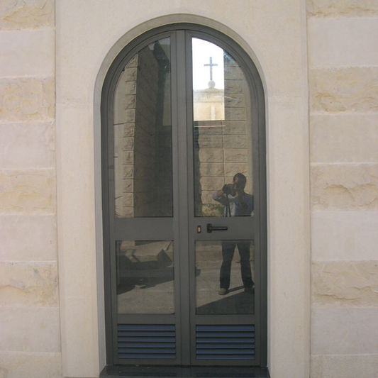 Portone ad arco in alluminio e vetro su parete in pietra.