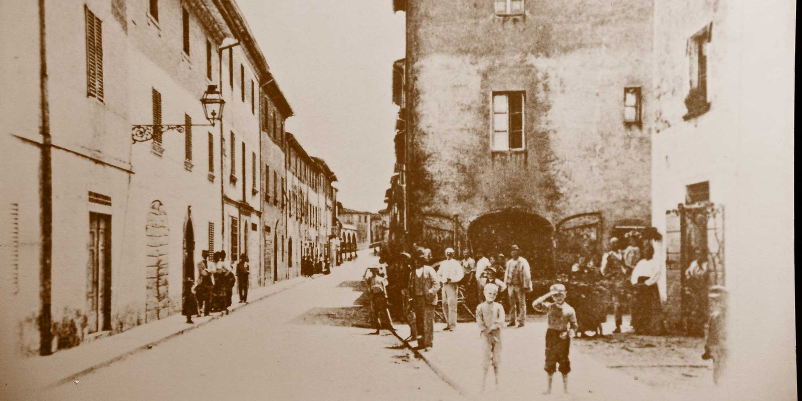 Antica foto seppia di una strada cittadina con persone.