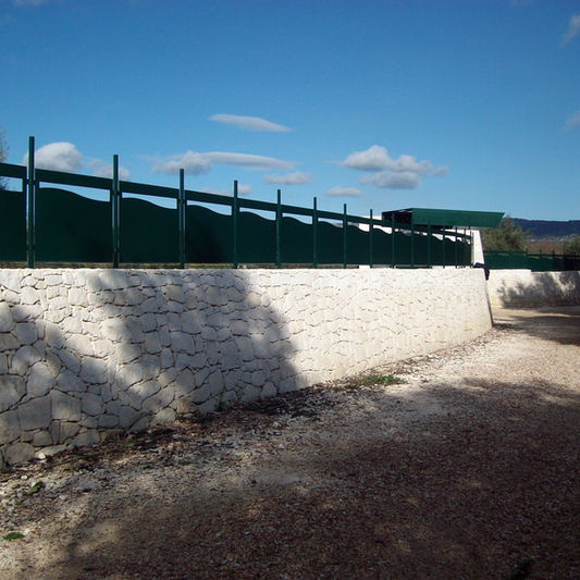 Muro di recinzione in pietra bianca con ringhiera verde.