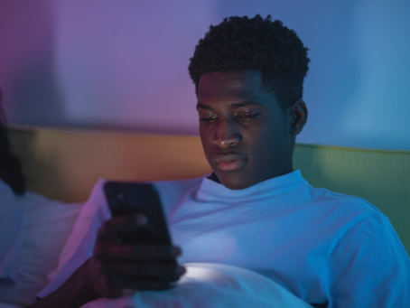 Man sitting in bed and looking at his phone in a dimly lit room