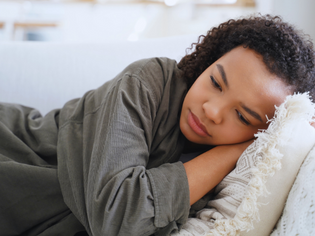 Teenage girl lying on a couch with her head resting on a pillow, appearing sad and withdrawn