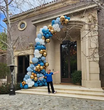 Lorena "Nina" Cesena standing by a blue and gold balloon arch at an entrance