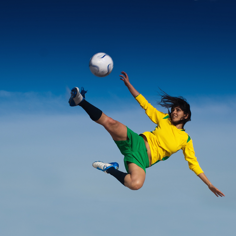A woman footballer kicking a football, whilst jumping in the air
