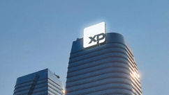 Prédio corporativo com fachada de vidro e placa iluminada “XP” no topo, sob céu azul.