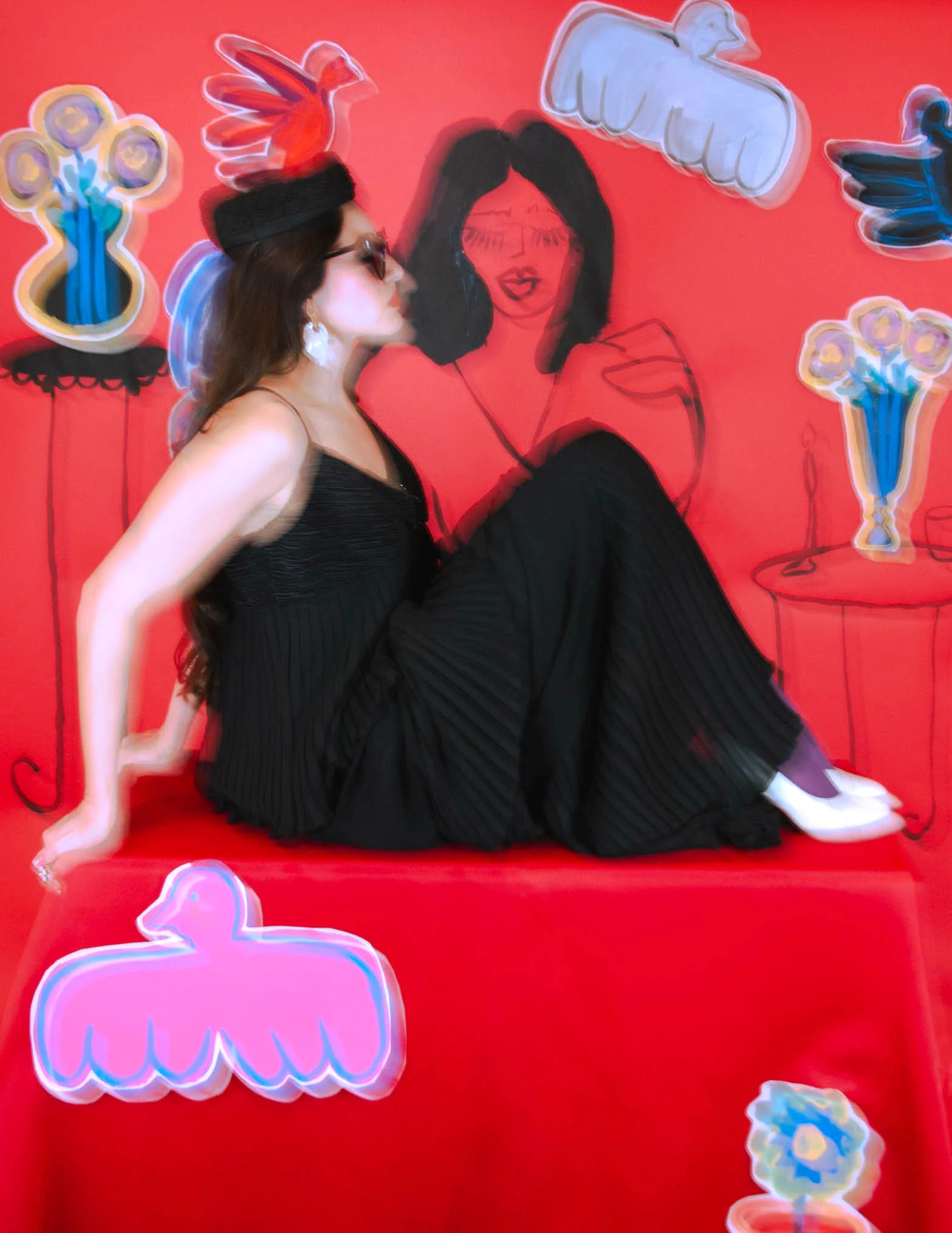 Persona con vestido negro y gorro posando contra un fondo rojo con ilustraciones coloridas de flores y aves