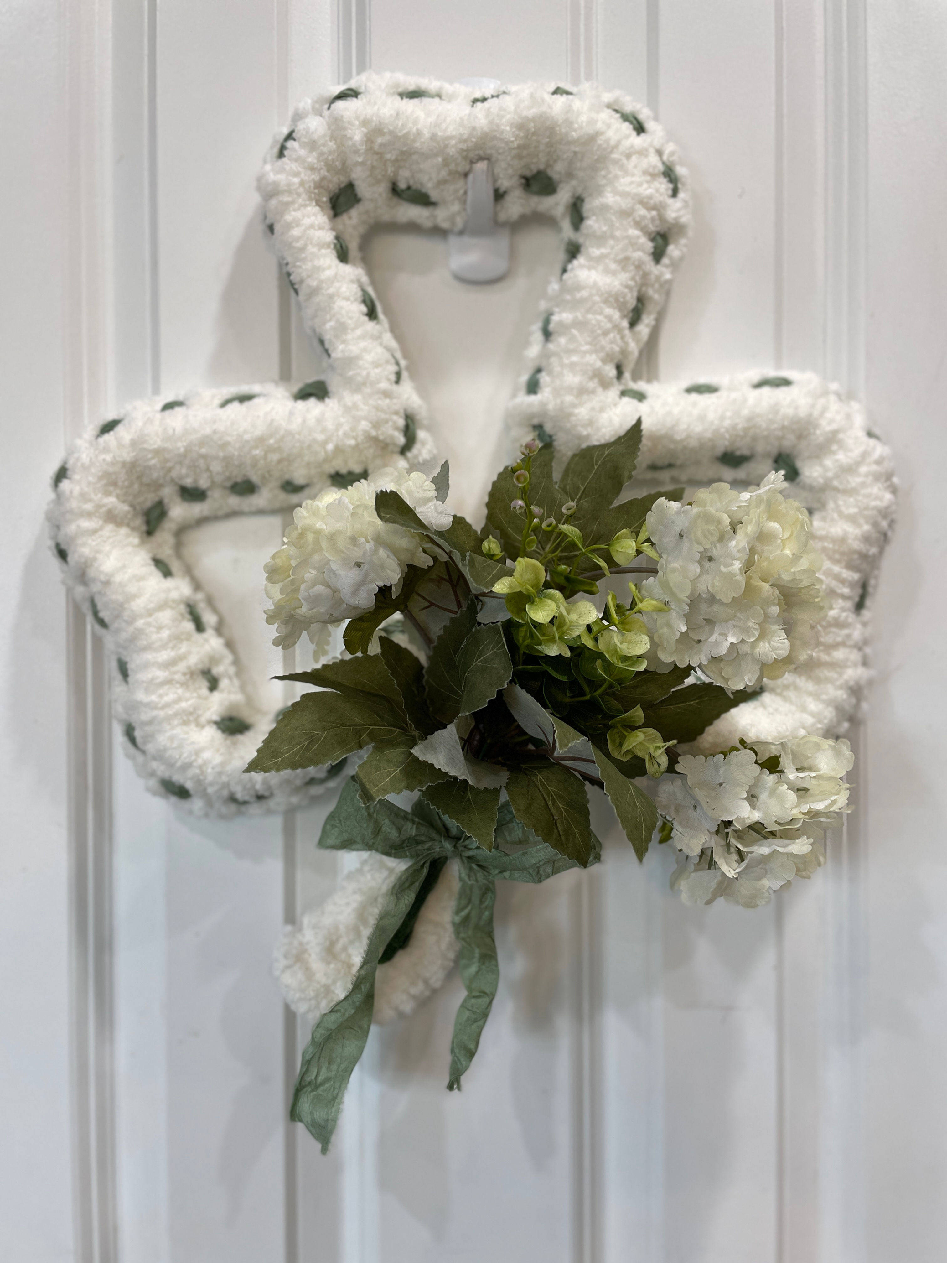 Beautiful farmhouse style St. Patty's Day wreath with clusters of white hydrangeas shown on a white door.
