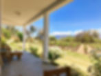 Porch overlooking vineyard rows, white flowers, trees, and mountains under a bright blue sky.