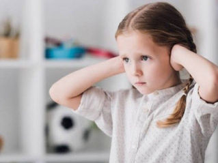 A young child covering their ears and looking overwhelmed by everyday noise at home in Lafayette CO