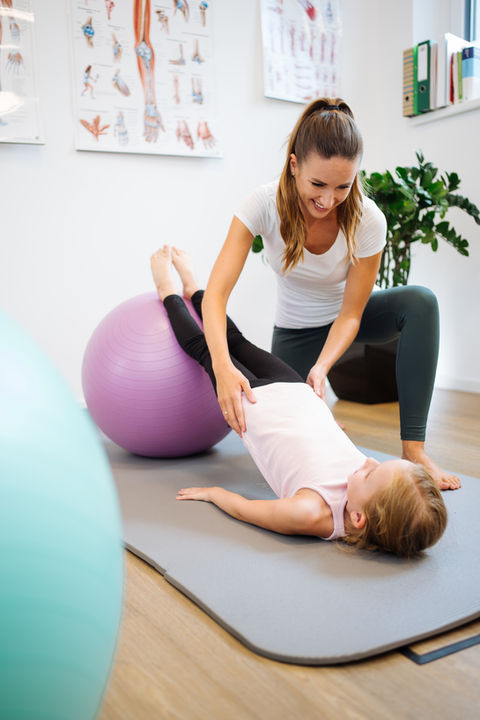 Kind macht Physiotherapie-Übungen mit Therapeutin