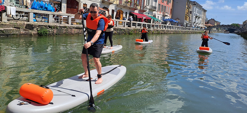 Tre persone praticano Stand Up Paddle (SUP) sui Navigli di Milano, indossando giubbotti salvagente