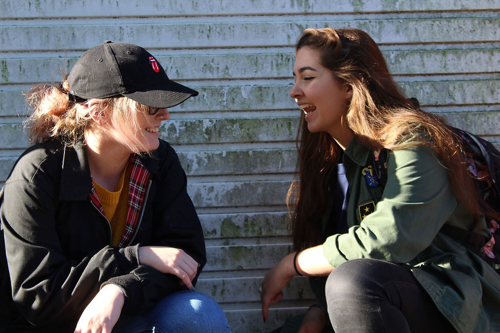 The author of 'Listen', Molly Farrenden, laughing with friend, Clare Sansome, crouched outside a garage door. Photo taken by Hannah-May Coull.
