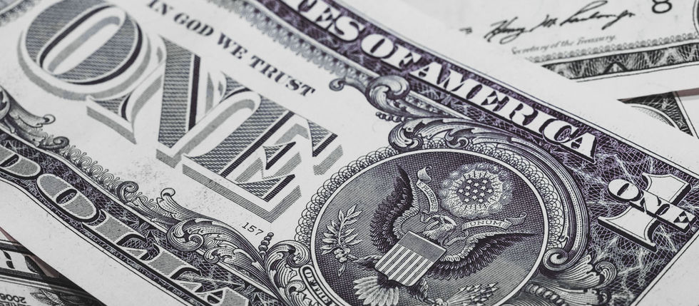 Close-up of overlapping U.S. one-dollar bills, showing ornate black-and-white details, purple seals, and IN GOD WE TRUST text.
