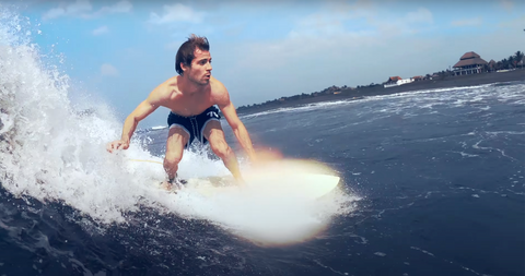 "A surfer skillfully rides a wave at El Paredón, Guatemala, with the beach and coastal buildings in the background."