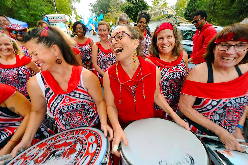 Group of female drummers in red uniforms laugh as they huddle together.