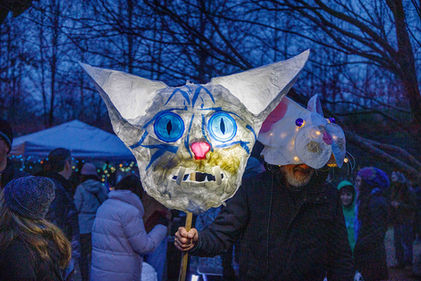 An illuminated blue and white cat head lantern held by a participant in a mouse mask.