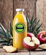 A bottle of Straight Juice's Summer Twist juice on a rustic wooden table, surrounded by fresh pineapples and red apples,