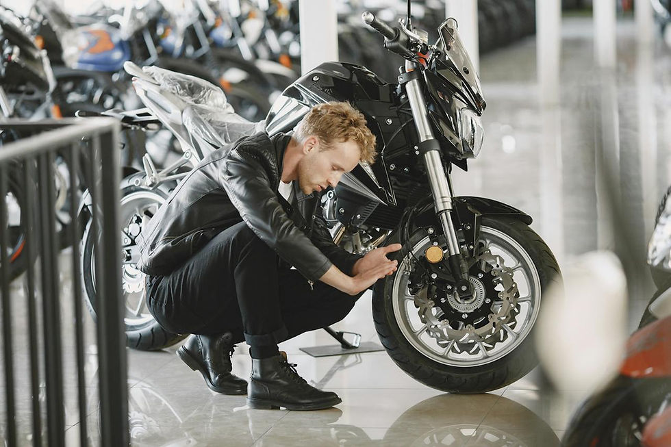 Man in leather jacket examines motorcycle wheel in showroom. Bikes line the background, reflecting on shiny floor, creating a focused mood.
