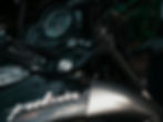 Close-up of a black motorcycle's dashboard and tank with "Pulsar" logo. The background is blurred, highlighting the metallic finish.