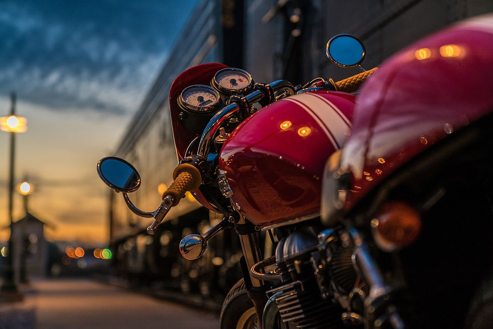 Close-up of a red motorcycle with striped tank, parked beside a train at sunset. Warm lighting creates a nostalgic mood.