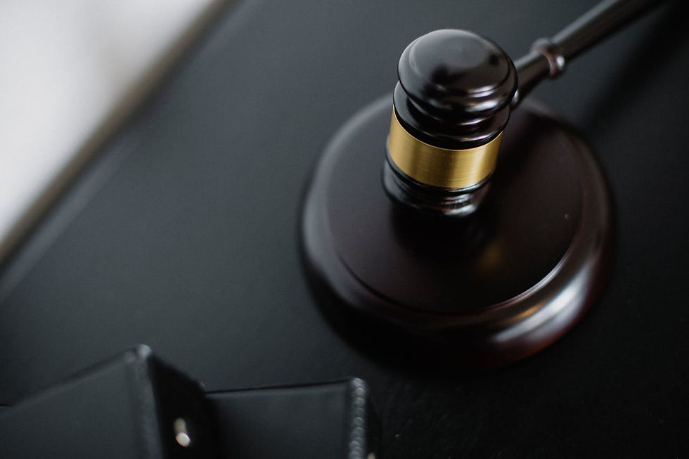 Close-up of a dark wooden gavel with a gold band on a black surface, symbolizing justice. A blurred black wallet is in the foreground.